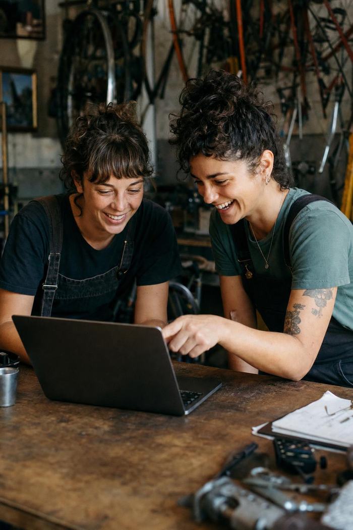 Deux associées d’un atelier de réparation de vélos regardent un ordinateur portable sur le comptoir